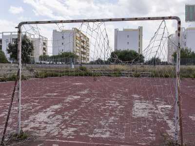 L'Accademia � ospitata  dalla �vecchia� scuola media del quartiere, ormai chiusa: una grande struttura per gran parte inutilizzata. Da un varco nella rete di recinzione raggiungiamo quella che era la �palestra all�aperto� dell�ex scuola. Ora non resta che il ricordo di un campo di calcio il cui stato � ben rappresentato dai brandelli di una rete